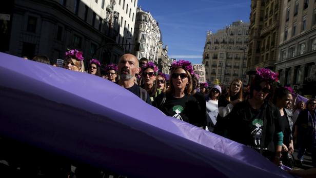 Eine Demonstration mit vielen Menschen, die lila Blumenkränze tragen und ein lila Banner halten.
