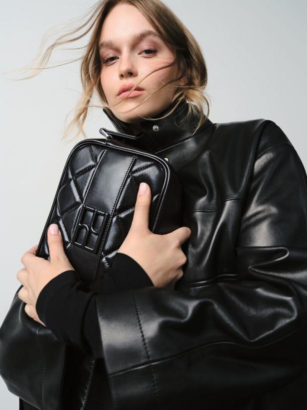 Eine Frau mit Lederjacke hält eine schwarze, gesteppte Handtasche.