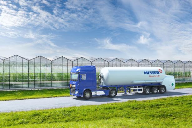 Ein weißer Tanklastwagen bewegt sich auf einer Straße neben einem Gewächshaus. Ein weißer Tanklastwagen bewegt sich auf einer Straße neben einem Gewächshaus.