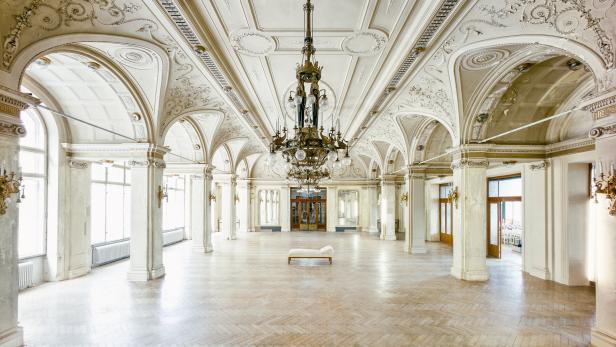 Prunkvoller Saal mit Parkettboden, Stuck an den Wänden, großen Fenstern und Lustern.
