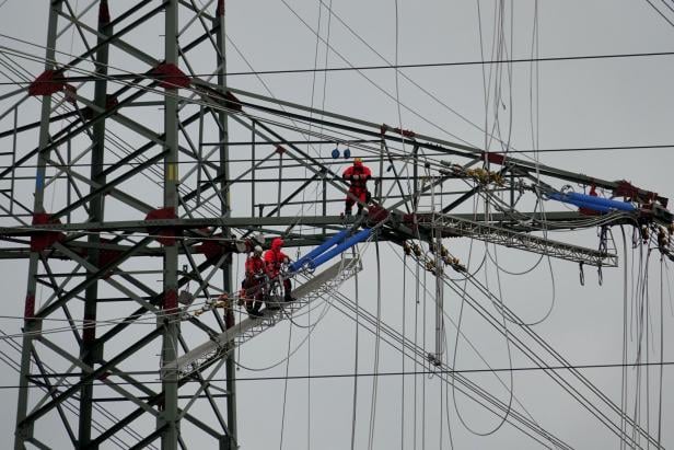 Strommast mit Arbeitern und vielen Leitungskabeln darauf.