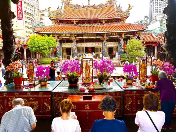 Der Longshan-Tempel in Taipeh mit Gläubigen und Blumenarrangements.