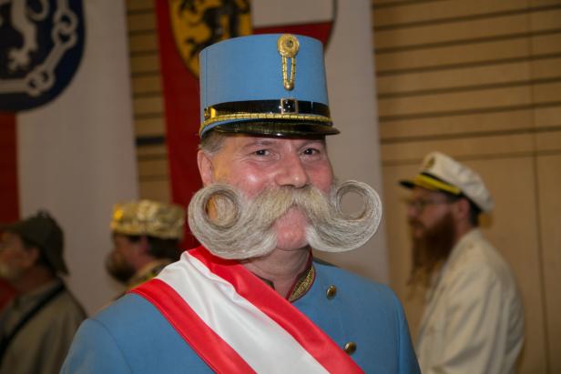 Ein Mann mit gezwirbeltem Schnurrbart, blauer Uniform und Schärpe.