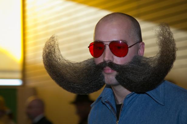 Ein Mann mit roter Sonnenbrille und einem sehr langen, gezwirbelten Bart.