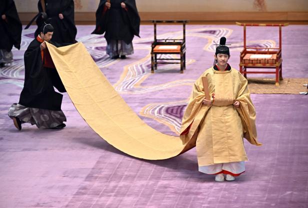 Prinz Hisahito Prinz Hisahito in traditioneller japanischer Kleidung schreitet feierlich, während eine zweite Person sein langes Gewand trägt.