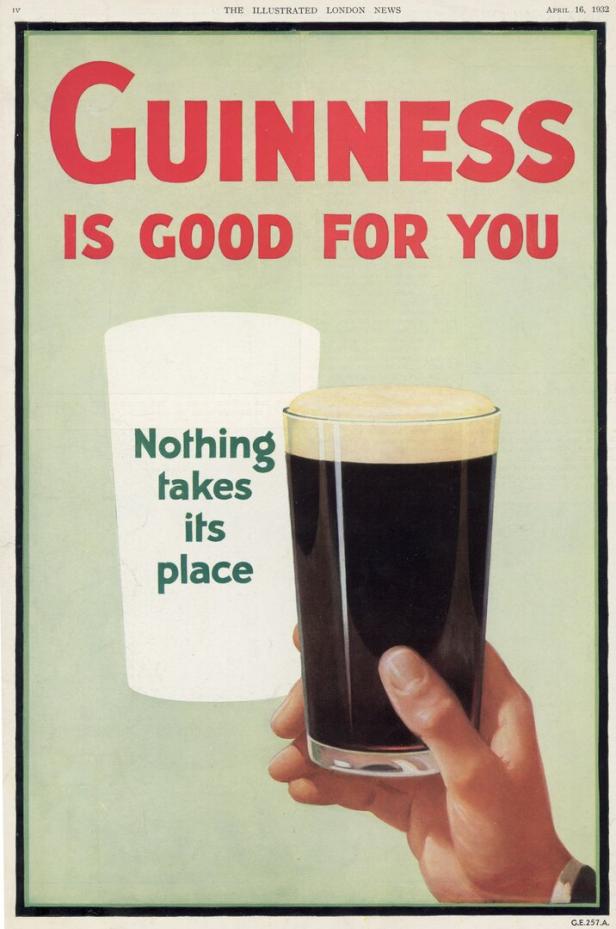 Eine Hand hält ein Glas Guinness vor einem Werbeplakat.