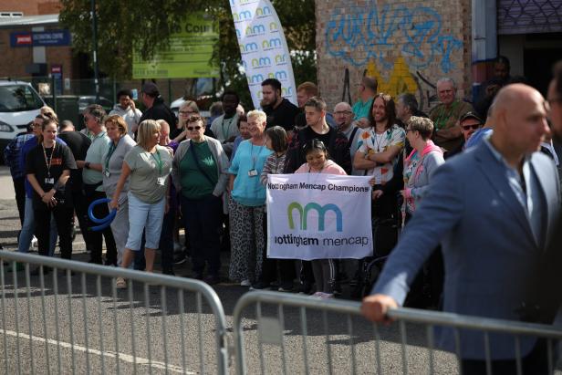 Eine Gruppe von Menschen steht hinter Absperrgittern, einige halten ein Banner mit der Aufschrift „Nottingham Mencap Champions“.