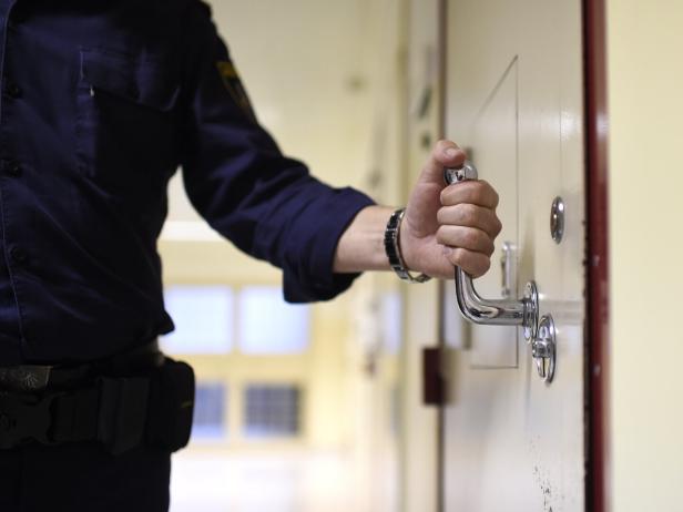 Eine Person in Uniform öffnet mit der rechten Hand eine schwere Tür mit Metallgriff in einem Flur.