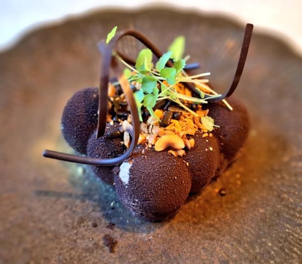 Ein Dessert mit Schokoladenüberzug, Nüssen und grünen Kräutern im Lokal De Fortuyne in Mechelen.