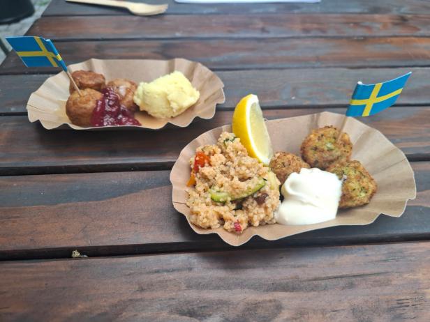 Zwei Speisen auf Papptellern, die ab Jänner 2026 bei Ikea neu am Speiseplan stehen: Falafel (im Vordergrund) mit Couscous, Gemüse und Aioli und Fleisch-und-Gemüse-Bällchen mit Erdäpfelpüree, Rahmsauce und Preiselbeeren.