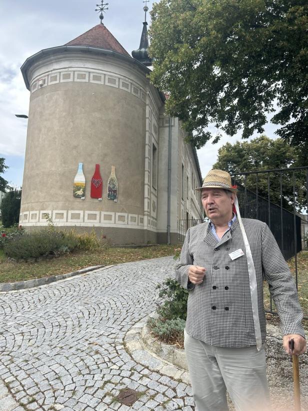 Ein Poysdorfer Kellergassenführer in typischer Montur, einer für Winzer üblichen Jacken und einem Hut mit Bändern, steht vor der Barbarakapelle in Poysdorf.