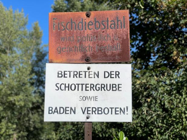 Ein rostiges Schild warnt vor Fischdiebstahl und verbietet das Betreten sowie Baden in einer Schottergrube.