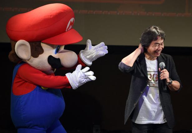 Shigeru Miyamoto mit einem Mario-Maskottchen auf einer Bühne.