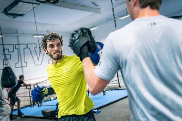 Ein Boxer mit gelbem T-Shirt trainiert mit einem Trainer in einer Turnhalle.