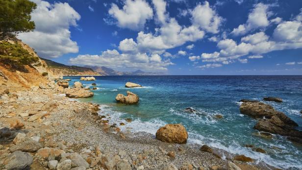 Ein felsiger Strand mit türkisfarbenem Wasser unter einem blauen Himmel mit Wolken.