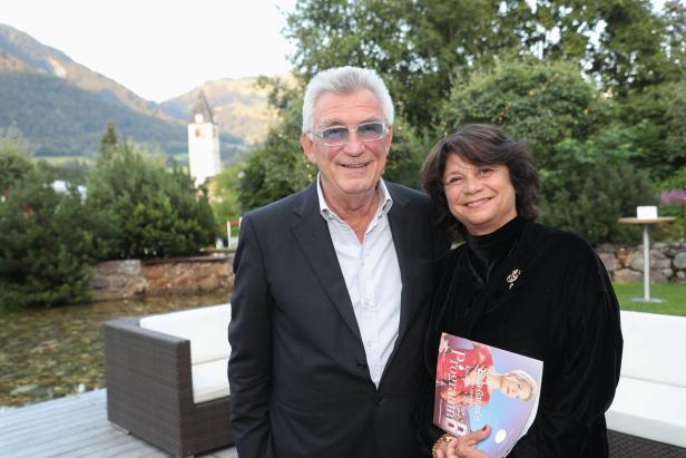 Ein Mann und eine Frau posieren vor einer Bergkulisse für ein Foto. Die Frau hält ein Programmheft „Klassik in Alpen“.