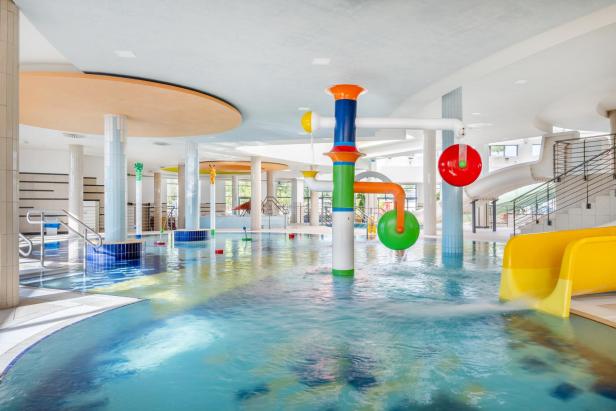 Eine Wasserrutsche in einem großen Innenpool, umgeben von Wasser und bunten Fliesen.
