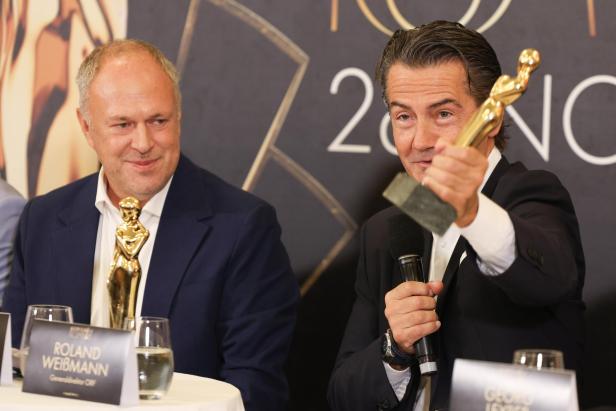 ++ HANDOUT ++ PRÄSENTATION/VOTINGSTART "KURIER ROMY 2025: GRASL / WEISSMANN Zwei Männer posieren mit einer goldenen Statue vor einem dunklen Hintergrund.