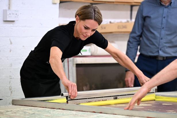 Prinzessin Kate bedient gemeinsam mit einer anderen Person ein Siebdruckgerät auf einem Arbeitstisch.