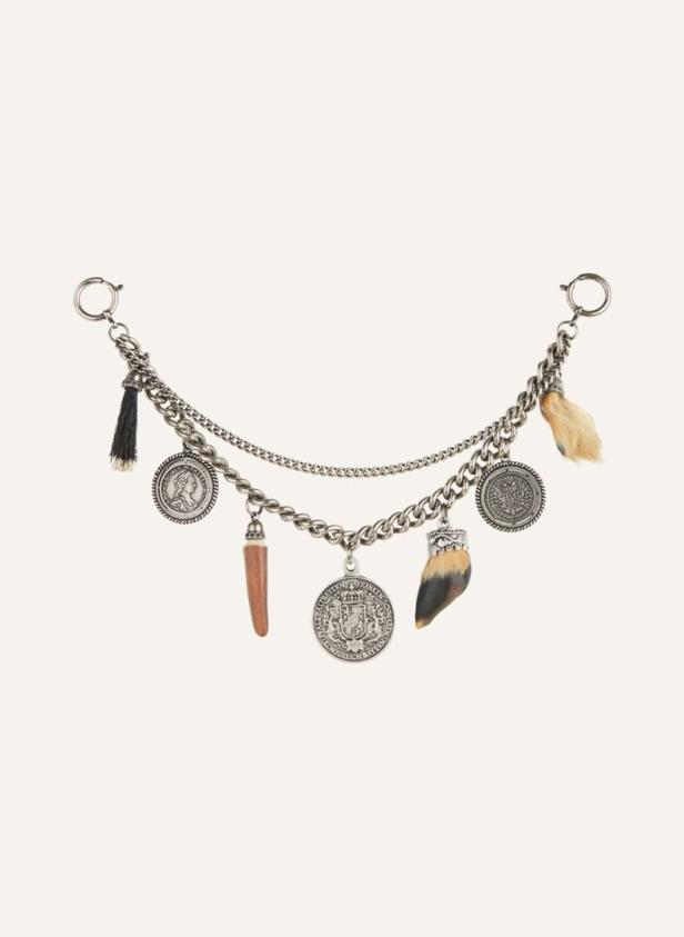 Eine silberne Kette mit Anhängern wie Münzen, einem Tierfuß und einem dunklen Quastenförmigen Anhänger.