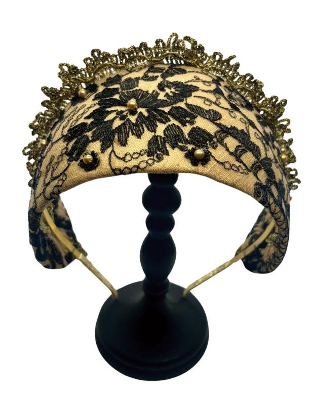Ein mit schwarzer Spitze und goldenen Perlen verzierter Haarreif auf einem schwarzen Ständer.