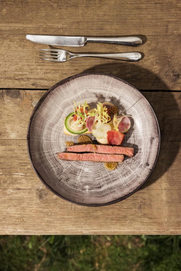 Ein Teller mit Rindfleisch, Gemüse und Senf auf einem Holztisch.
