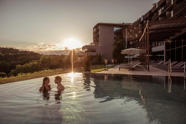 Ein Paar entspannt im Pool des Falkensteiner Balance Resort Stegersbach bei Sonnenuntergang.