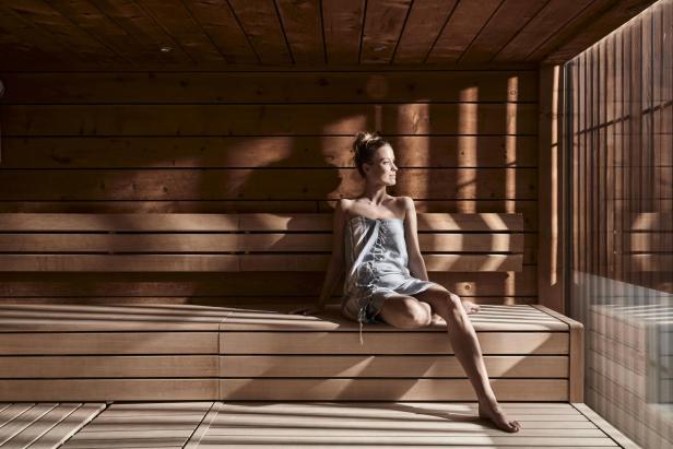 Eine Frau sitzt in einem Handtuch gehüllt in der Sauna des Falkensteiner Balance Resort Stegersbach.