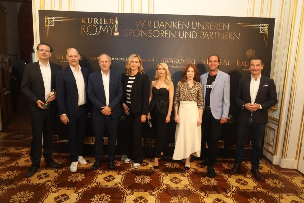 Eine Gruppe von Personen posiert vor einer Wand mit dem Schriftzug „Kurier Romy“. Eine Gruppe von Personen posiert vor einer Wand mit dem Schriftzug „Kurier Romy“.