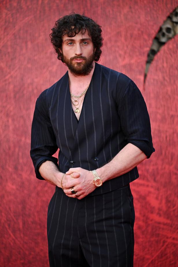Aaron Taylor-Johnson posiert vor einem roten Hintergrund.