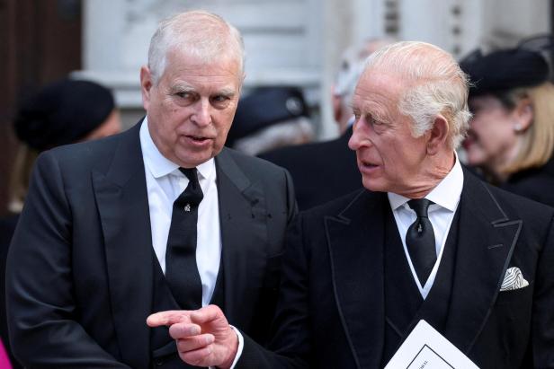 König Charles und Prinz Andrew unterhalten sich in dunklen Anzügen, wobei Andrew gestikuliert.