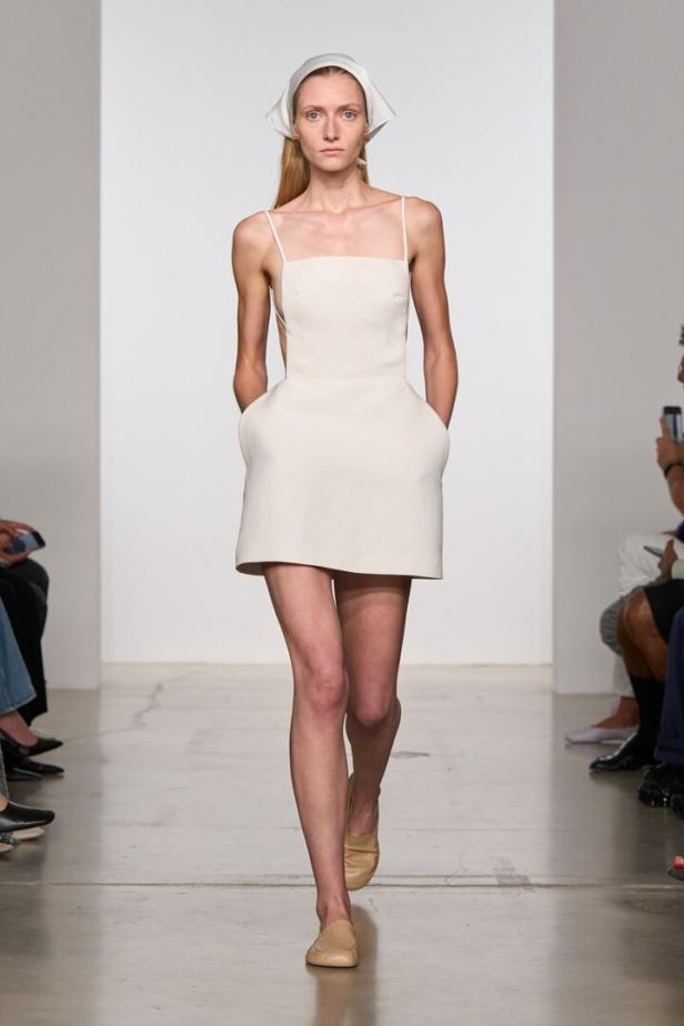 Eine Frau mit Kopftuch und kurzem, weißen Kleid auf einem Laufsteg.