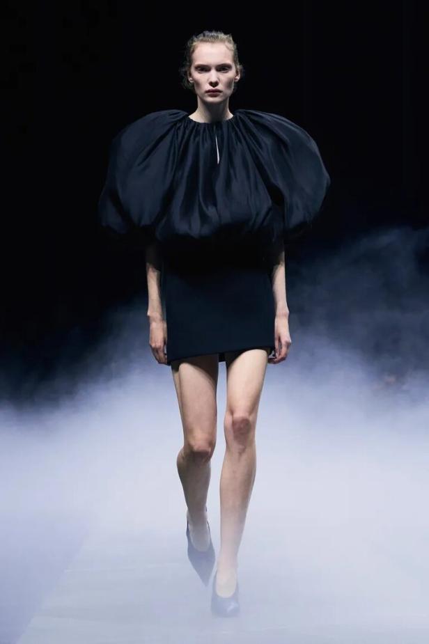 Eine Frau in einem schwarzen Kleid mit Puffärmeln auf einem Laufsteg.