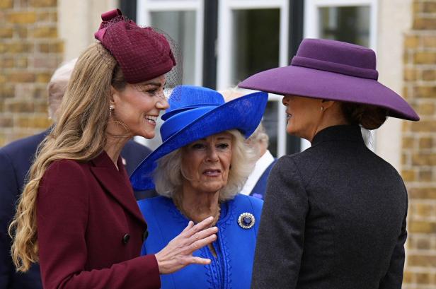 Prinzessin Kate, Königin Camilla und Melania Trump sind elegant gekleidet mit auffälligen Hüten und unterhalten sich im Freien.