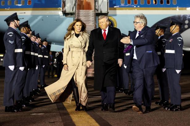 Donald Trump und Melania verlassen ein Flugzeug, flankiert von Soldaten und einem Mann im Anzug.