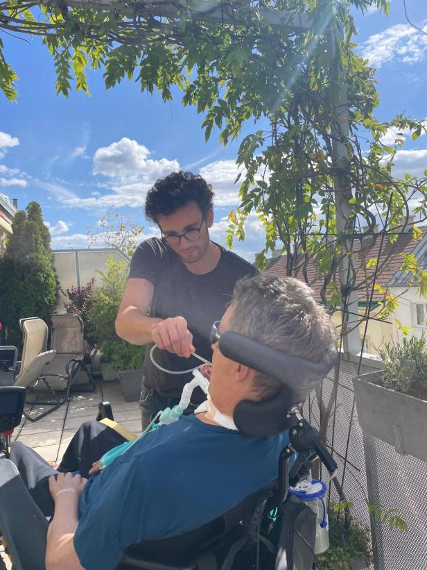 Pfleger Martin kümmert sich um einen Patienten im Rollstuhl auf einer Terrasse. Pfleger Martin kümmert sich um einen Patienten im Rollstuhl auf einer Terrasse.