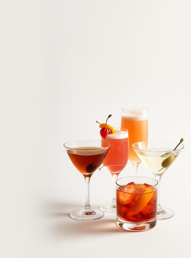 Fünf verschiedene Cocktails, darunter ein Martini und ein Aperol Spritz, stehen auf einem Tisch.