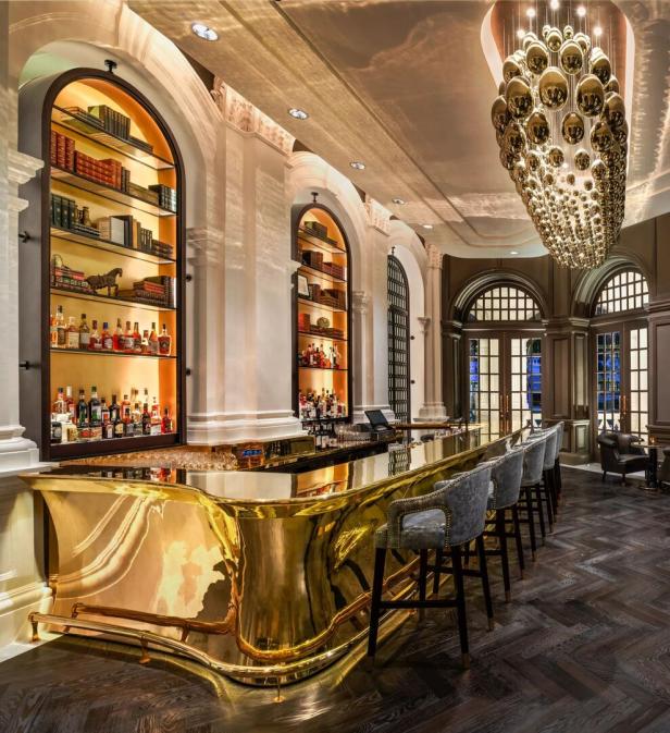 Eine Bar mit einer goldenen Theke und beleuchteten Regalen mit Büchern und Spirituosen.