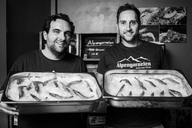 Zwei Männer präsentieren Schalen mit „Alpengarnelen“ auf Eis.