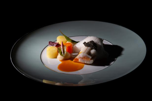 Ein Teller mit Fisch, Kaviar, Kartoffeln und einer hellen Soße wird präsentiert.