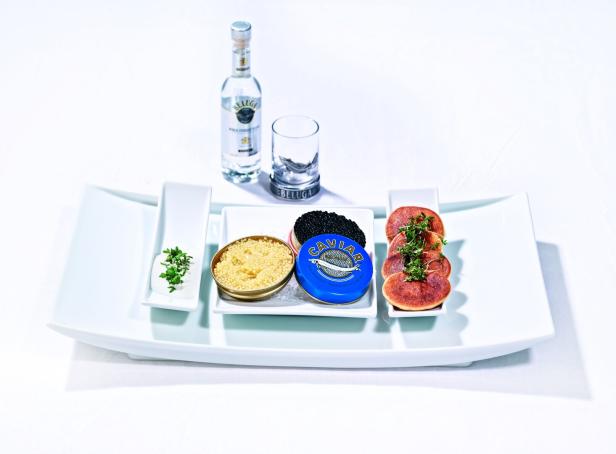 Kaviar, Blinis, saure Sahne und eine Flasche Beluga-Wodka auf einem weißen Tablett.