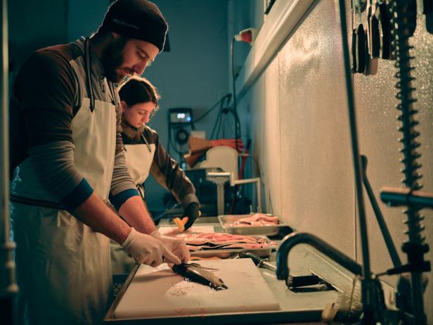 Zwei Personen in Schürzen bereiten Fisch in einer Küche zu.
