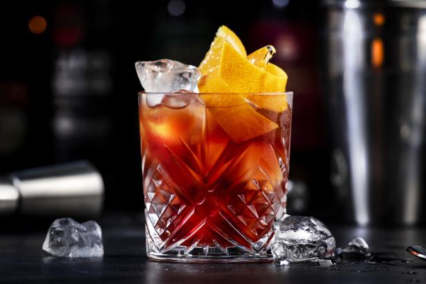 Ein Espresso Negroni Cocktail mit Gin, Wermut, Espresso, Kaffeelikör, Orangenscheibe und Eiswürfeln auf einer Bar.