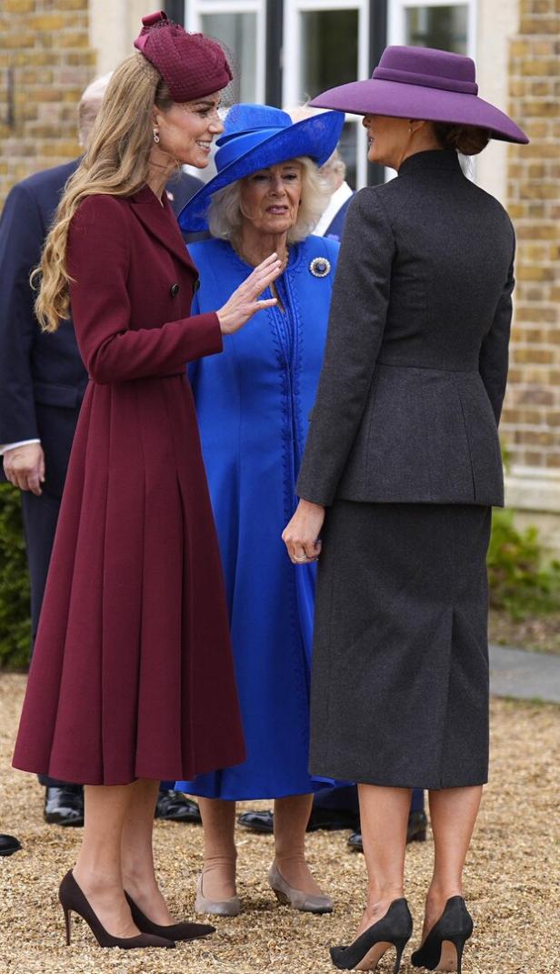 Prinzessin Kate, Königin Camilla und Melania Trump unterhalten sich draußen, jede trägt einen farblich abgestimmten Mantel und passenden Hut.