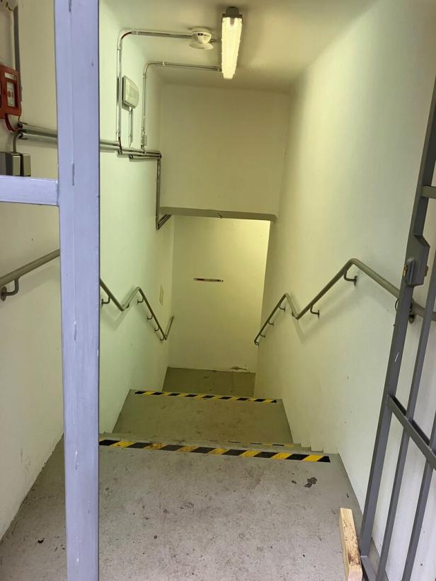 Ein Treppenabgang mit gelb-schwarzen Warnstreifen führt in einen Kellerraum.