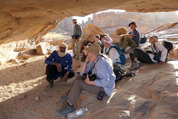 Trekking-Gruppe rastet in der Wüste Algeriens unter einem Felsvorsprung.