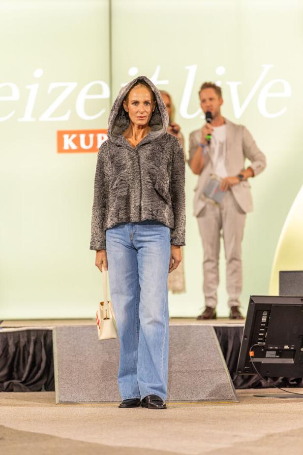 Eine Frau mit Kapuzenjacke und Jeans steht auf einer Bühne.