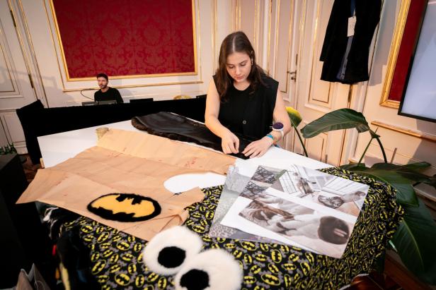 Eine Frau arbeitet an einem Tisch mit Stoffen und Schnittmustern, darunter ein Batman-Logo.