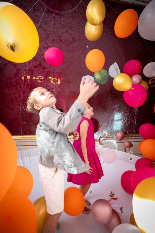 Zwei Kinder spielen in einem Raum voller bunter Ballons.