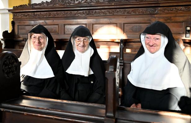 Drei Nonnen sitzen in einer hölzernen Kirchenbank.